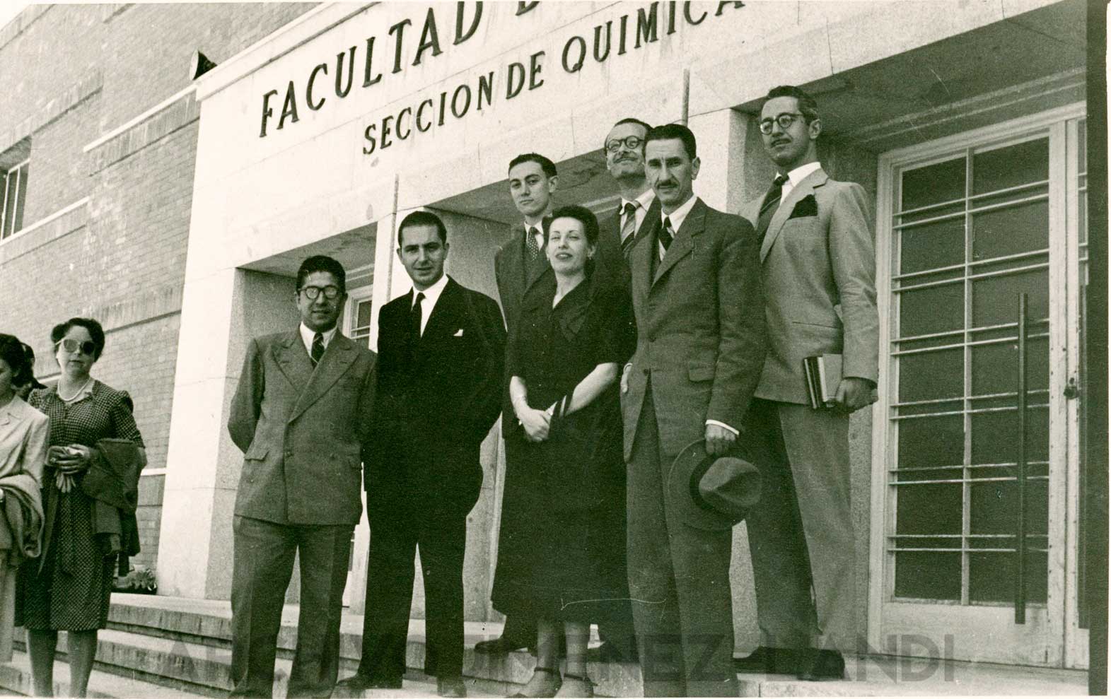 FFMTV-FAJL-001 Vintage black and white photo showing 6 men in suits on a staircase posing around a woman holding her hands in front of her