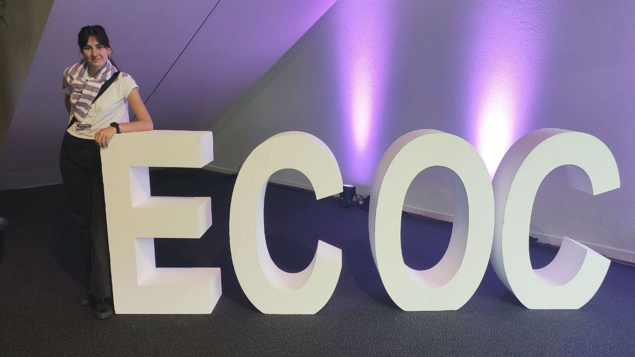 ECOC-InesCaceresPablo Inés Cáceres Pablo in front of the ECOC initials of the congress