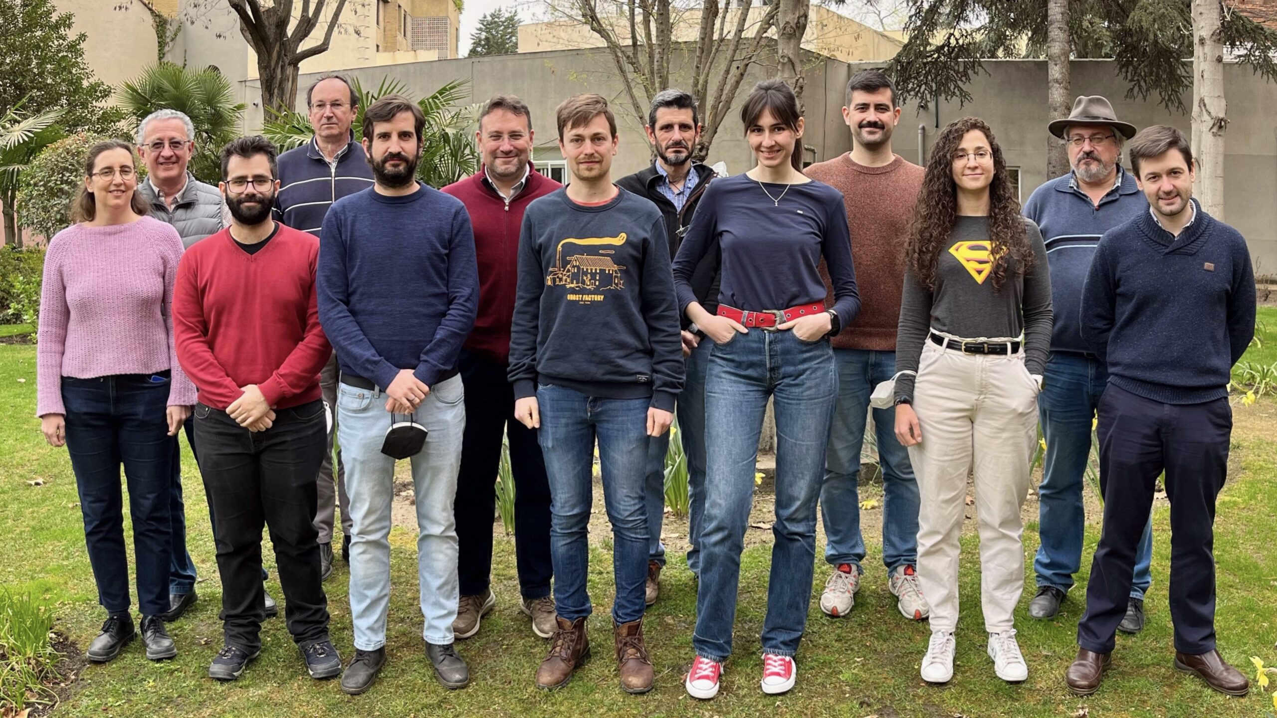 foto-grupo-N2GO-2022 Thirteen people posing in two rows in a garden with a wall in the background