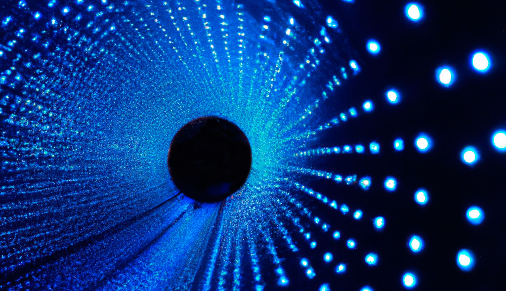 DALL·E-un-tubo-infinito-en-el-que-dentro-hay-pequeñas-esferas-luminosas Dentro de un tunel oscuro con multitud de puntos luminosos de color azul por las paredes